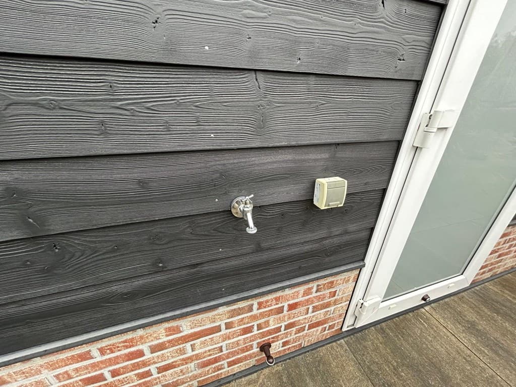 Klein gedeelte van de buitenmuur met een kraan en een elektrische aansluiting naast een deur met glazen panelen