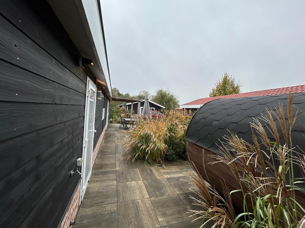 Steenachtige vloer met een zwart huis aan de linkerkant en een houten object aan de rechterkant, omringd door planten.
