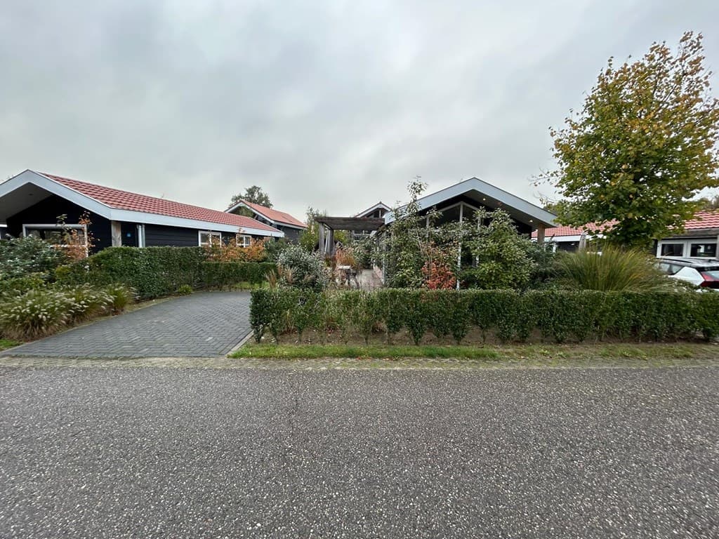 Buitenzicht op vakantiewoning met tuin, oprit en omliggend groen in een rustige wijk met meerdere woningen.