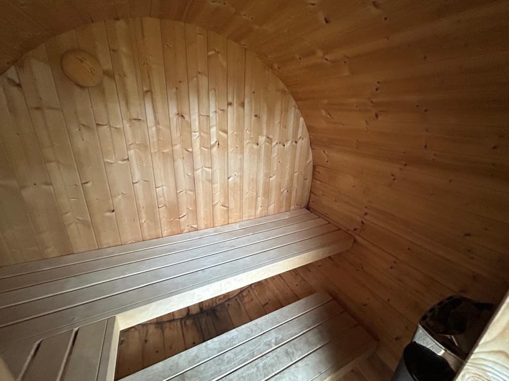 Sauna met houten wanden en banken, voorzien van twee smalle ligplaatsen en een afvalbak in de hoek.