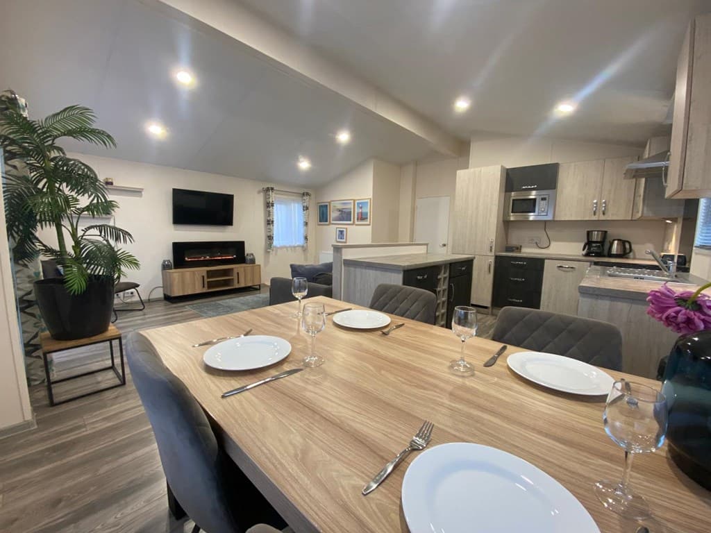 Eetkamer met een houten tafel, stoelen, moderne keuken en woonkamer met bank en tv aan de muur