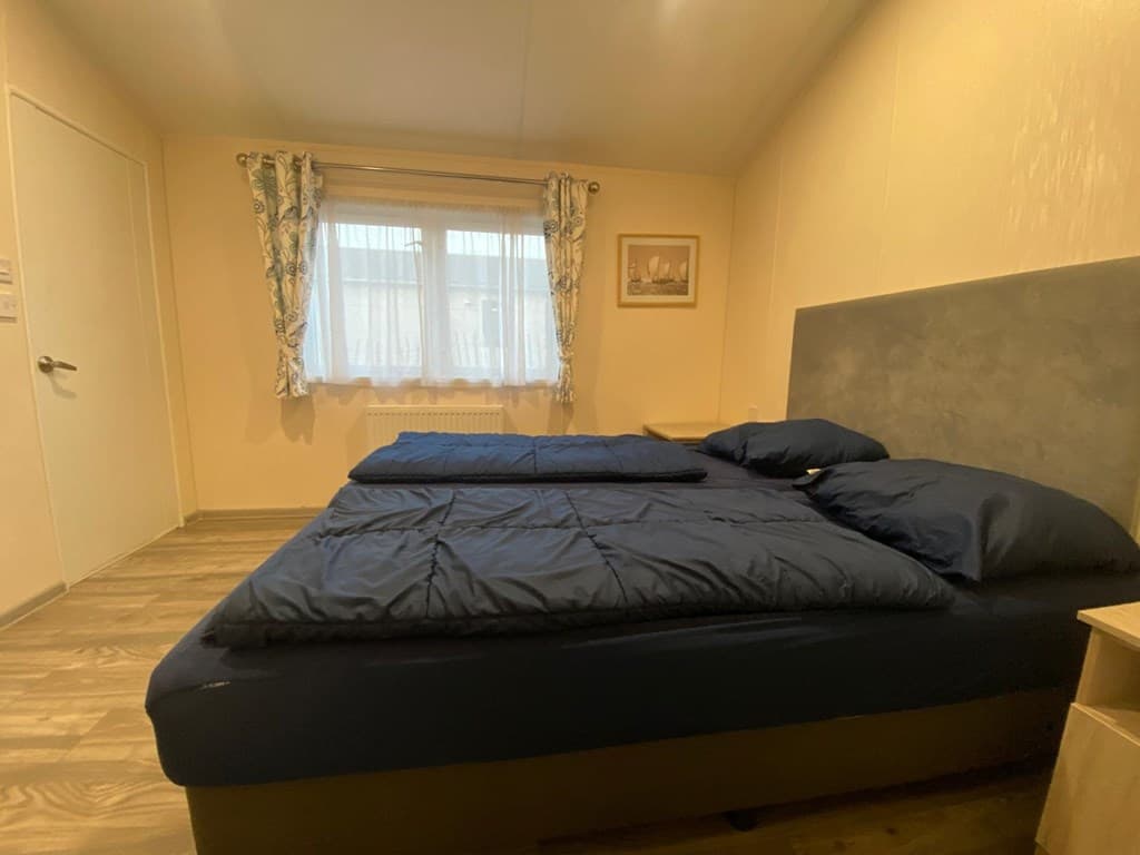 Slaapkamer met twee aparte bedden, een raam met gordijnen en een kastje naast het bed.