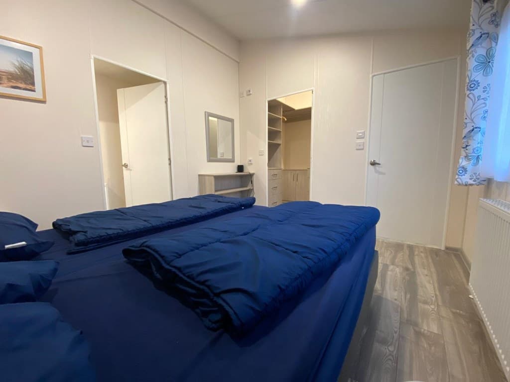 Slaapkamer met twee losse bedden, een spiegel, kledingkast en deur naar een andere ruimte.