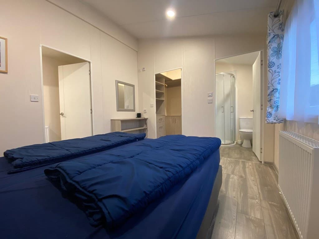 Slaapkamer met twee eenpersoonsbedden, kast, spiegel en toegang tot badkamer met douche en toilet.
