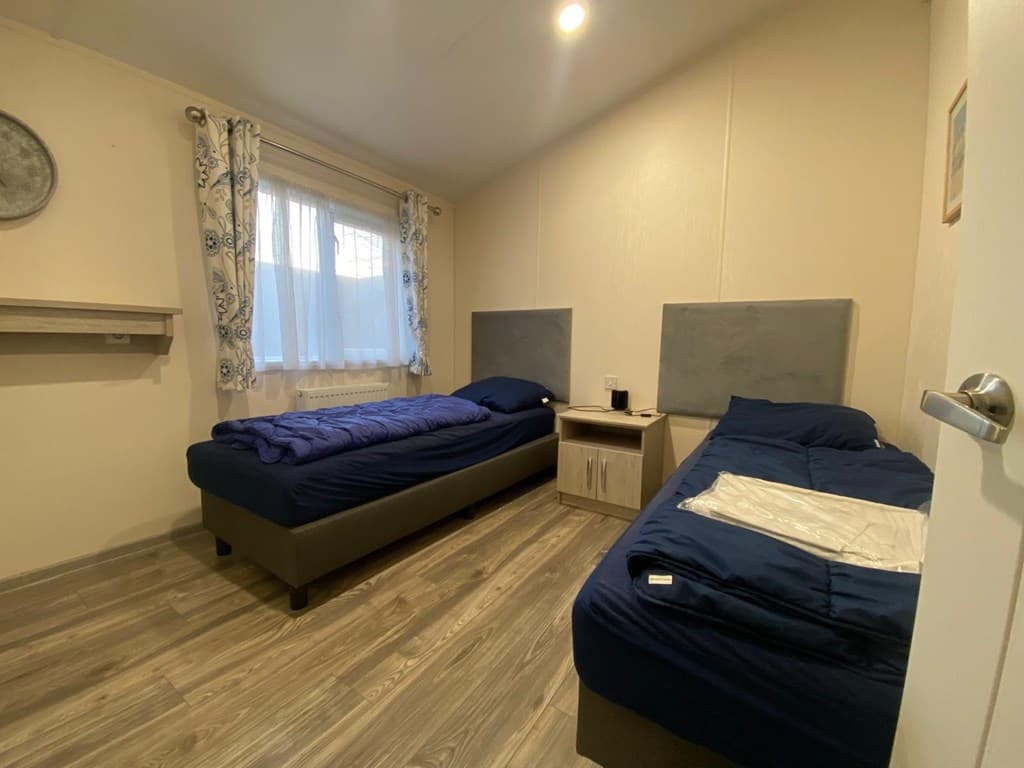 Slaapkamer met twee eenpersoonsbedden, lichtkleurige muren en een raam met gordijnen.