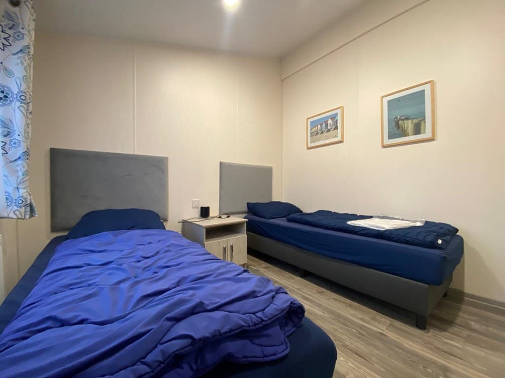 Twee eenpersoonsbedden met blauwe dekbedden in een lichte slaapkamer met schilderijen aan de muur.