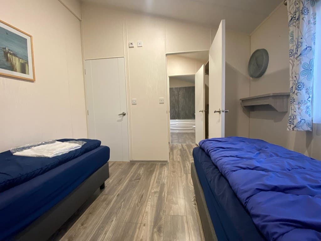 Slaapkamer met twee eenpersoonsbedden en een deur naar een andere ruimte, lichte wanden en laminaatvloer