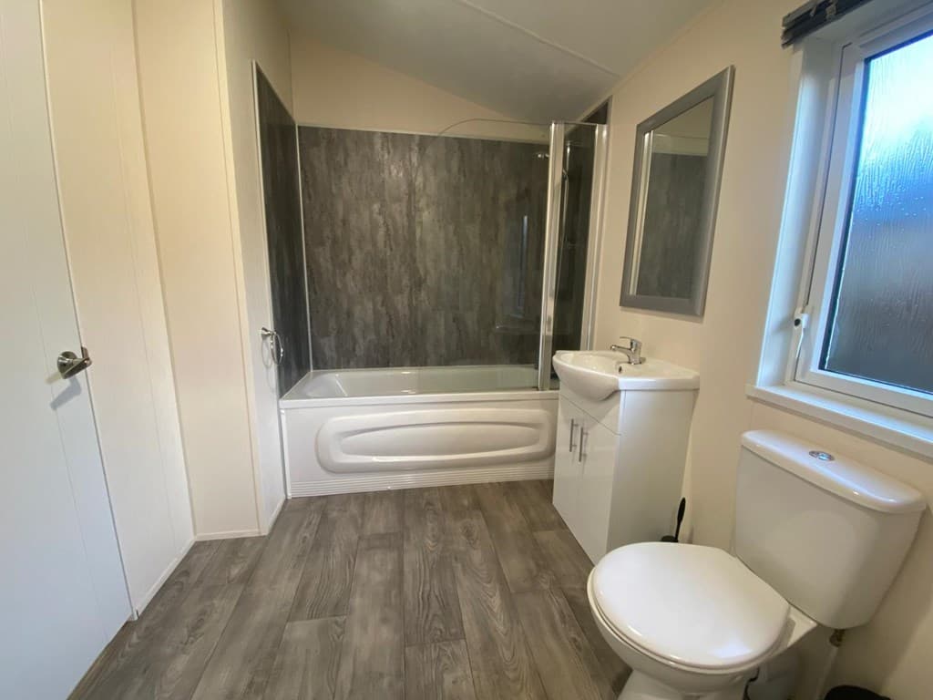 Badkamer met bad, douche en wastafel, lichte wanden en een vloer in houtlook