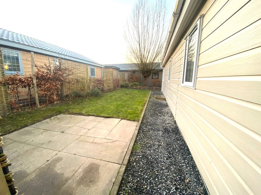 Tuin met gras en betegeld pad, omgeven door houten schuttingen en planten aan de zijkanten van de woning