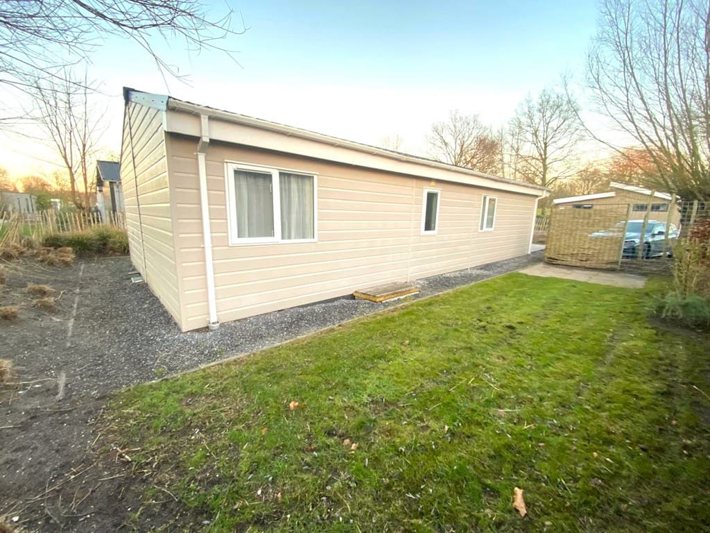 Vakantiewoning met lichtgekleurde gevel, ramen en grasveld aan de zijkant, gelegen in een rustige omgeving.