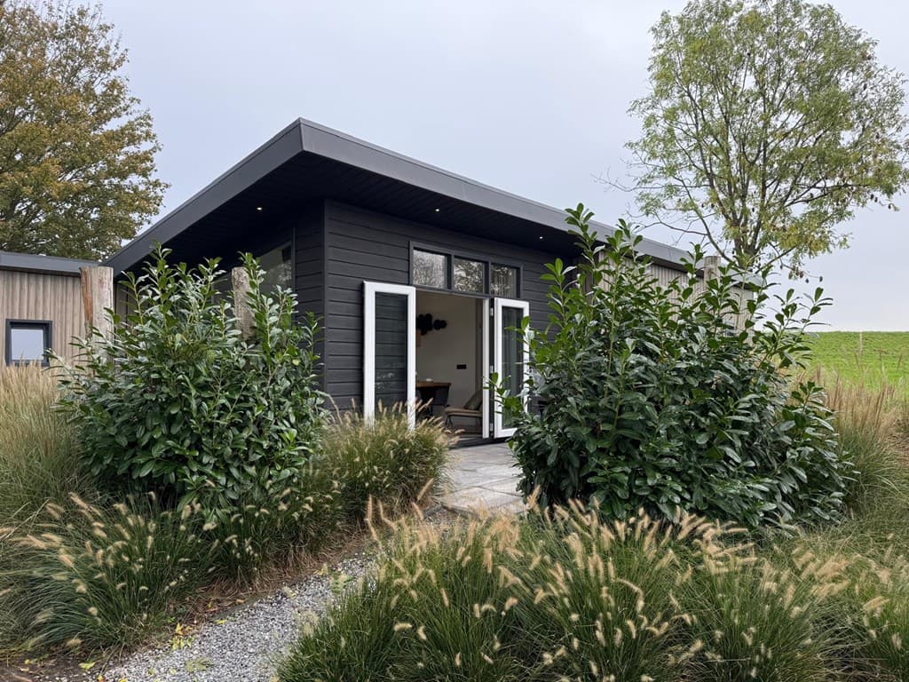 Moderne vakantiewoning omgeven door groene struiken en gras, met een betegeld pad naar de entree.