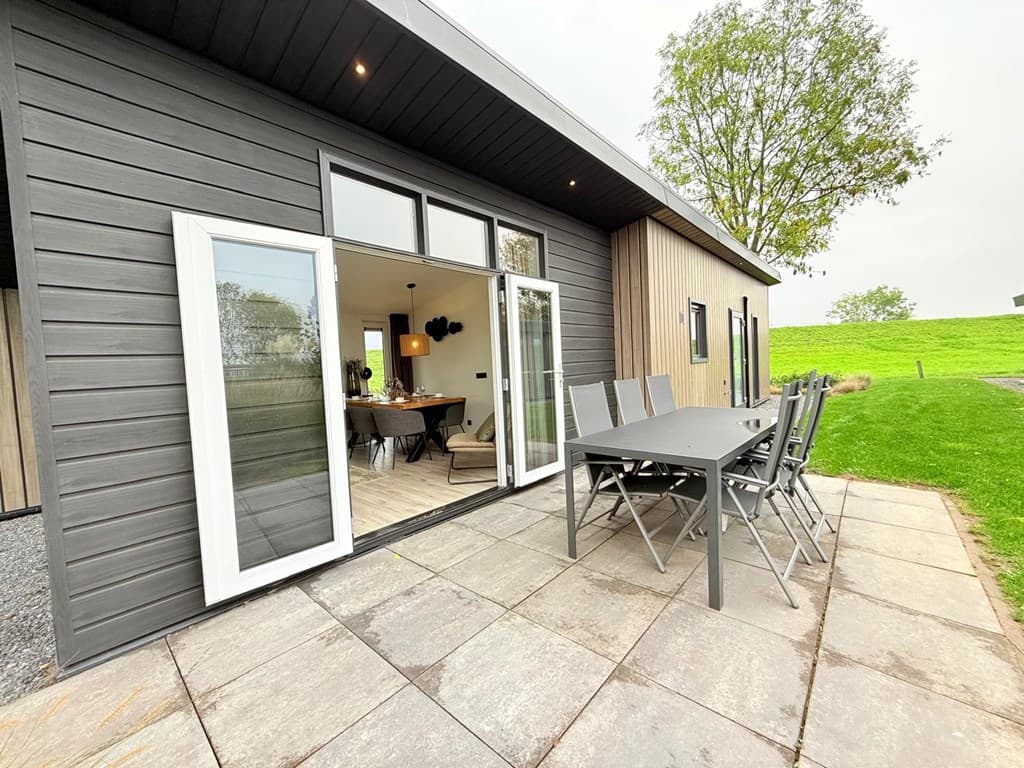 Terras met eettafel en stoelen, moderne woning met grote ramen en groene omgeving, grasveld op de achtergrond