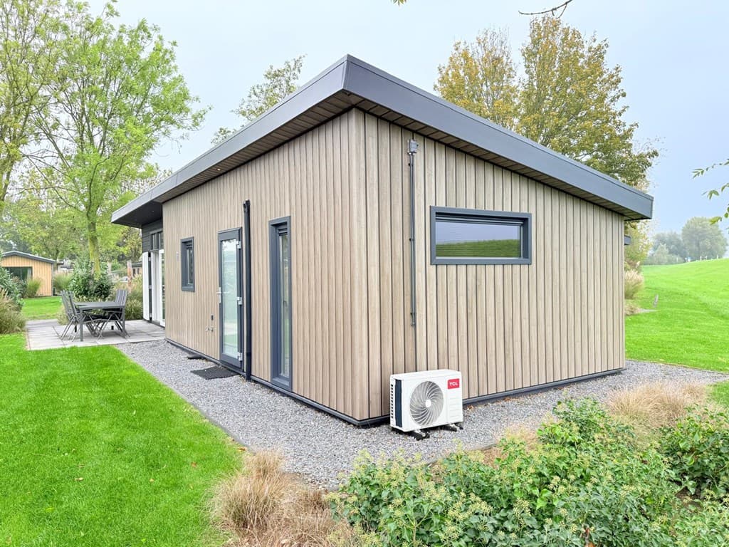 Moderne vakantiewoning met houten gevel, grote ramen en een terras met tuinmeubilair op een groene locatie