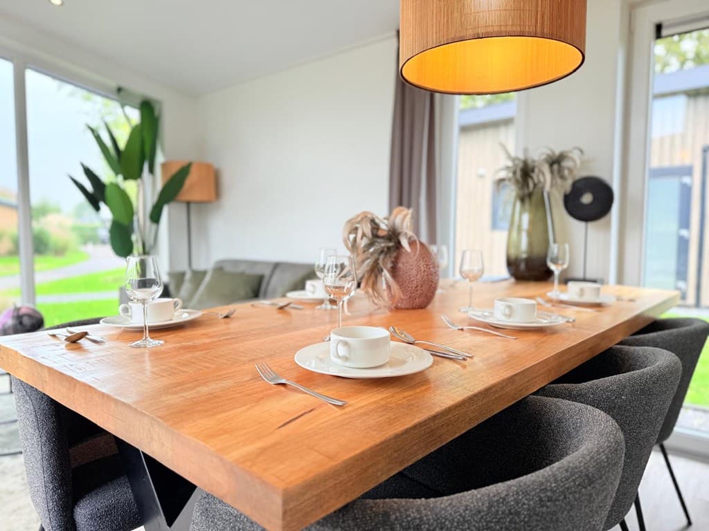 Tafelschikking met servies en glazen rondom een grote houten tafel, met moderne stoelen en stijlvolle decoratie.