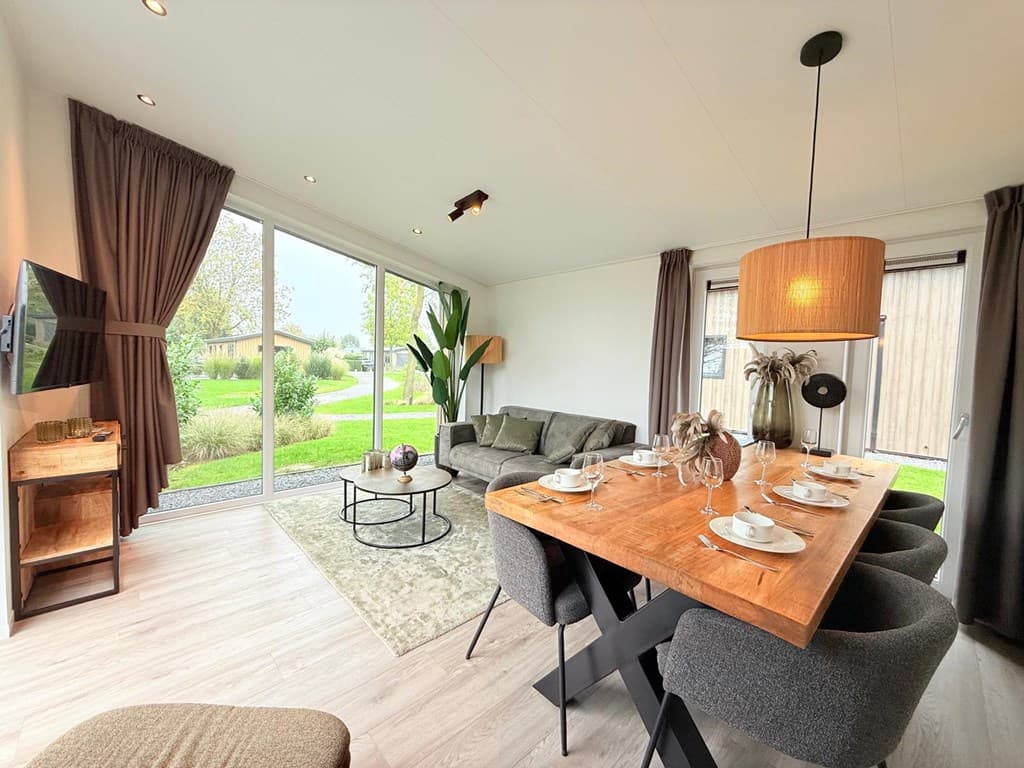 Moderne woonkamer met eettafel, bank en grote ramen met uitzicht op de tuin en omgeving