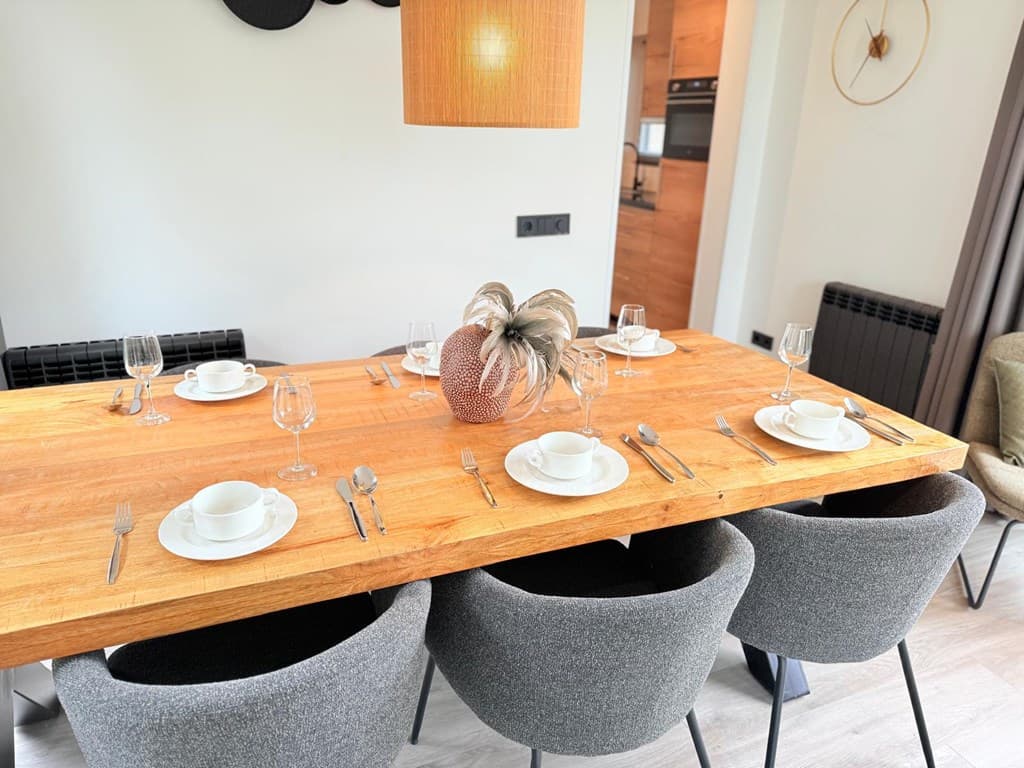 Eetkamer met een grote houten tafel, zes stoelen, en gedekte plaatsen met borden en glazen.