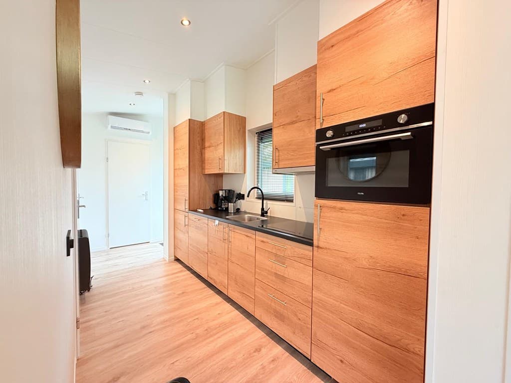 Moderne keuken met houten kasten, zwart aanrechtblad en inbouwapparatuur zichtbaar, lichte omgeving met laminaatvloer