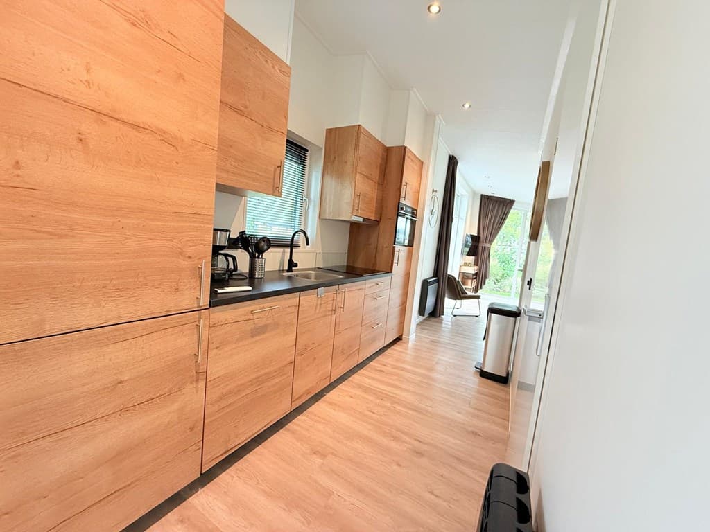 Moderne keuken met houten kasten, een koffiezetapparaat en uitzicht op de woonkamer met grote ramen.