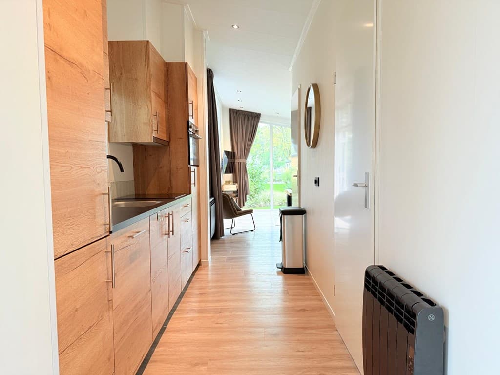 Ingang van een moderne woning met een open keuken en zicht op een zithoek met grote ramen en uitzicht op groen.