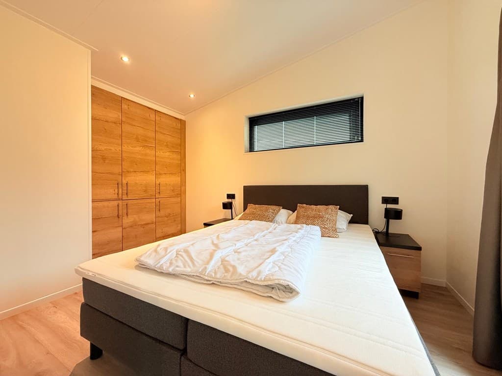 Slaapkamer met een tweepersoonsbed, houten kastenwand en sfeervolle wandlampen aan beide zijden van het bed