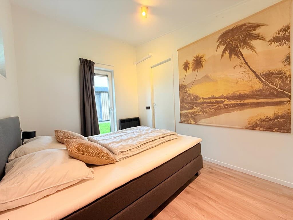 Slaapkamer met tweepersoonsbed, een groot schilderij van een landschap en een deur naar de buitenruimte.