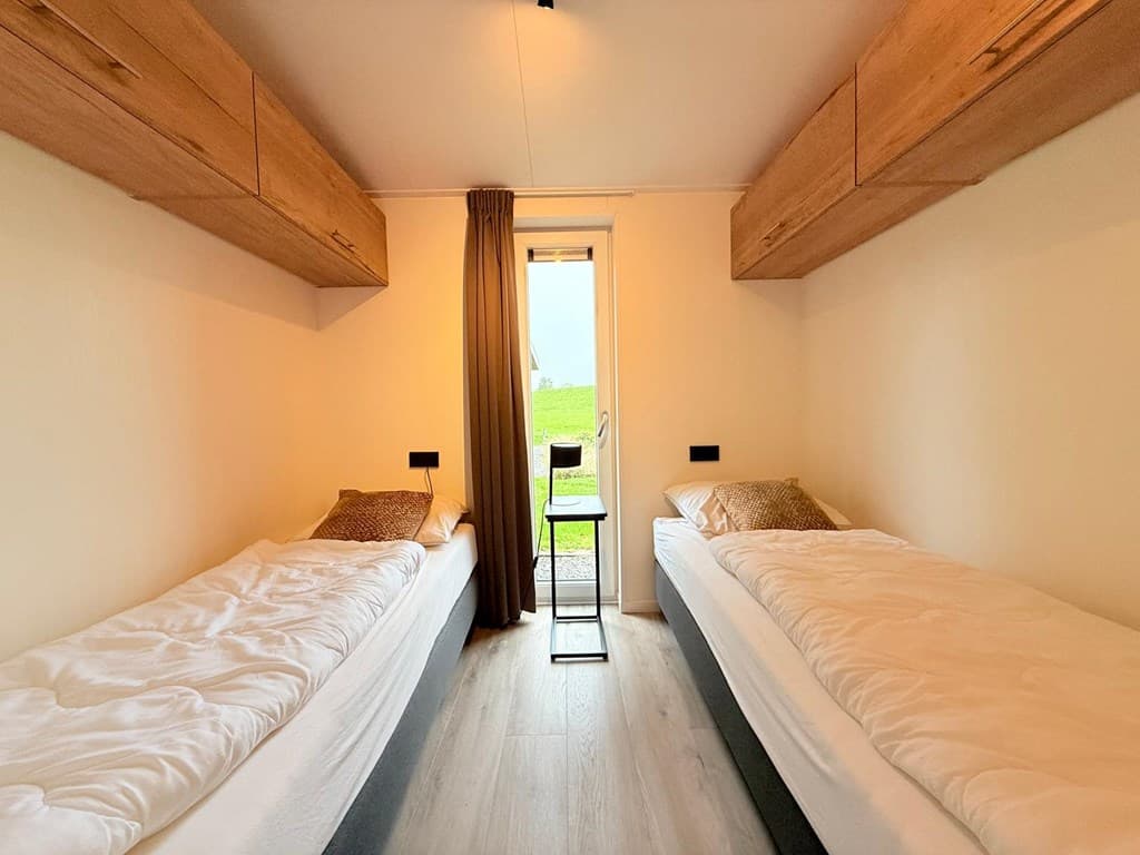 Slaapkamer met twee eenpersoonsbedden, lichtinval vanuit de deur en bovenkasten voor opbergruimte.