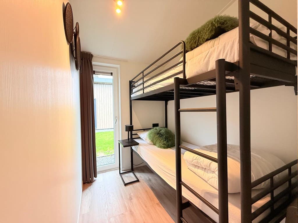 Slaapkamer met stapelbed, bureau en toegang tot buiten door een glazen deur.