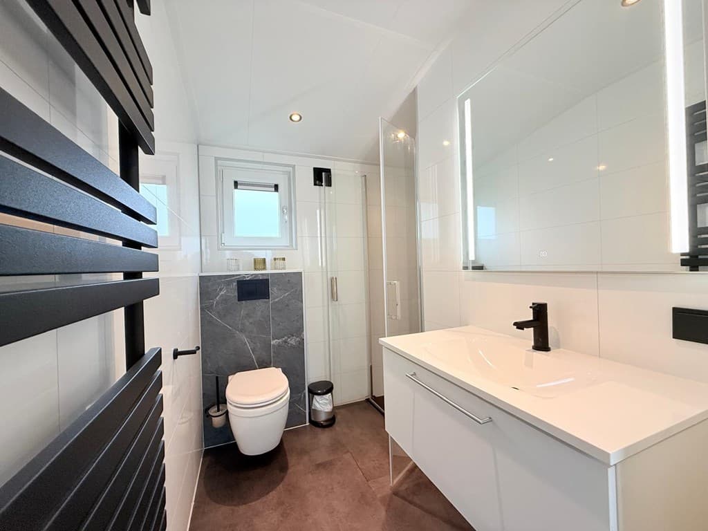 Moderne badkamer met toilet, inloopdouche, wastafel en grote spiegel, afgewerkt met lichte en donkere elementen