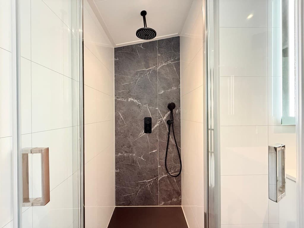 Douche met moderne regendouchekop, zwart wandpaneel en witte tegels aan de zijkanten.