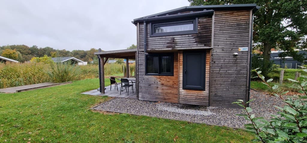 Houten vakantiehuisje met veranda, grasveld en struiken in EuroParcs Zuiderzee, omgeving van Biddinghuizen.