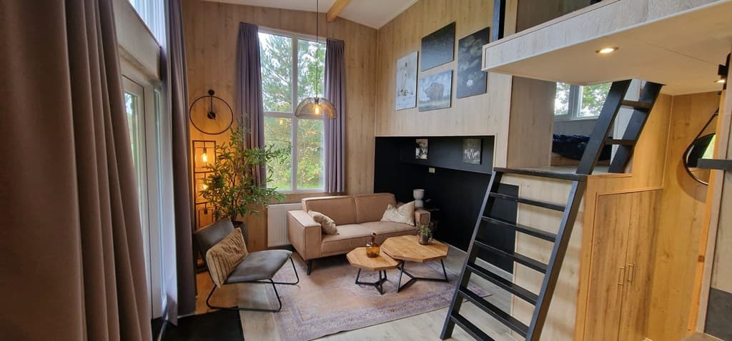 Licht en moderne woonkamer met loungebank, houten tafels en trap naar de bovenverdieping in EuroParcs Zuiderzee.
