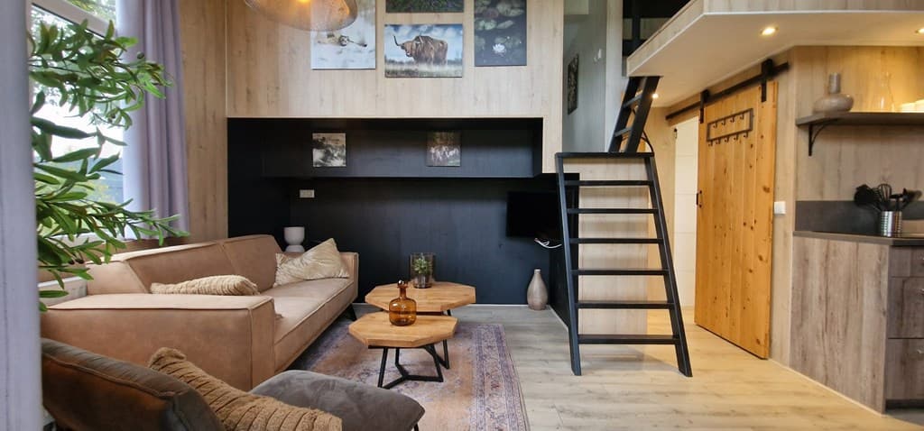 Moderne woonkamer met een bank, houten salontafels en een open trap naar de bovenverdieping in EuroParcs Zuiderzee