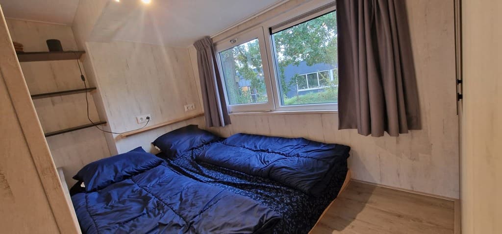 Slaapkamer met twee enkele bedden en ramen met uitzicht op de buitenruimte, neutrale houten afwerking en gordijnen.