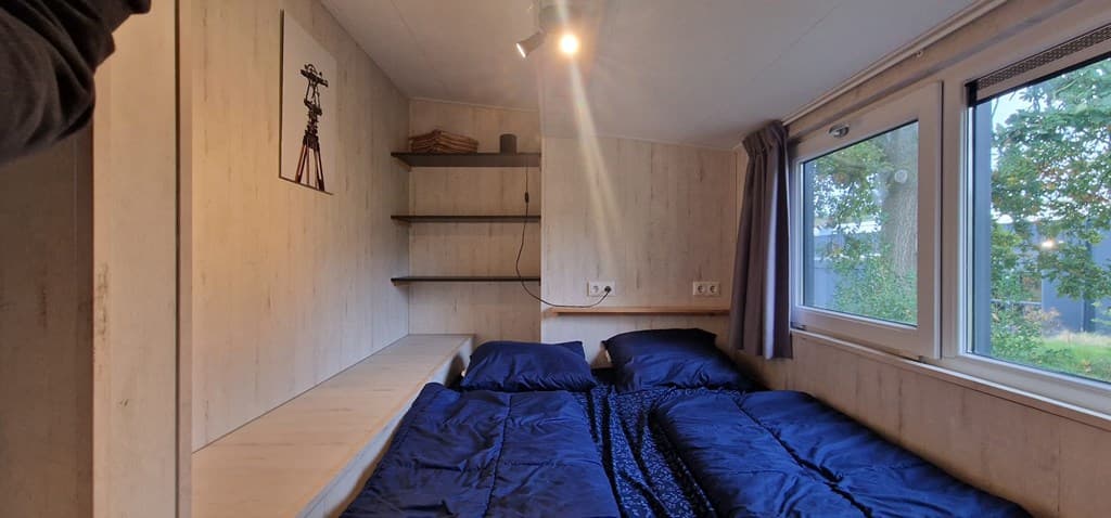 Slaapkamer met twee eenpersoonsbedden, een wandplank en ramen met uitzicht op groen.