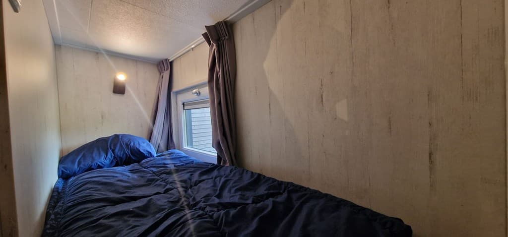 Slaapruimte met een eenpersoonsbed, raam met gordijnen en een wandlicht aan de zijkant.