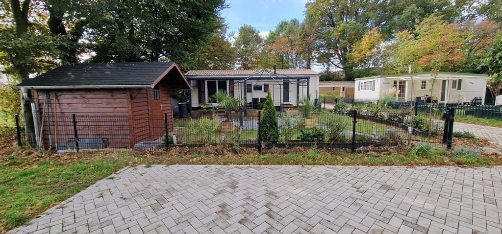 Tuin met een houten chalet, omheind perk met planten en een caravan op Camping De Spaendershorst B.V., Esbeek.