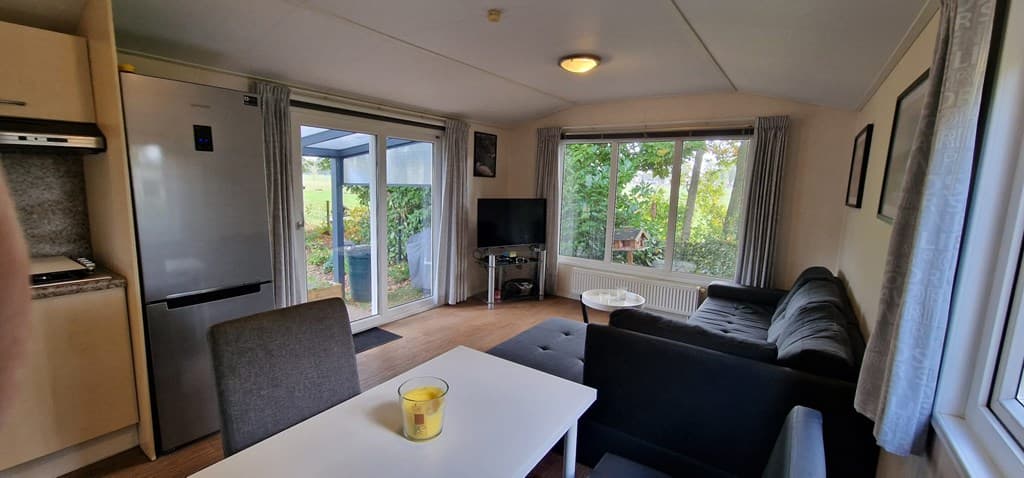 Gezellige woonkamer met keuken, televisie en zitplaatsen, veel natuurlijk licht door ramen en zicht op de tuin.
