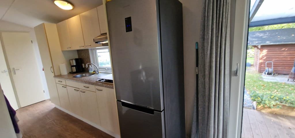 Moderne keuken met een grote koelkast, aanrecht en kasten, met toegang tot een houten terras buiten.
