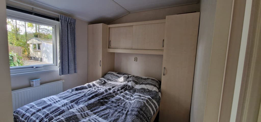 Sfeervolle slaapkamer met een tweepersoonsbed en kasten, groot raam met uitzicht op de buitenruimte