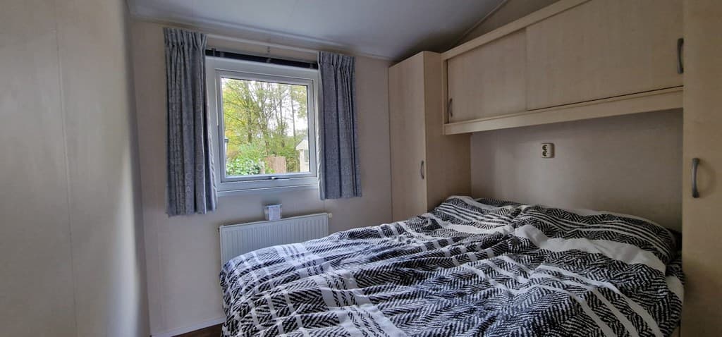 Slaapkamer met tweepersoonsbed, raam met uitzicht op groen en eenvoudige kastinrichting.