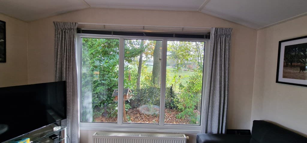 Uitzicht vanuit een woonkamer met een groot raam dat uitkijkt op een groene tuin met struiken en bomen.