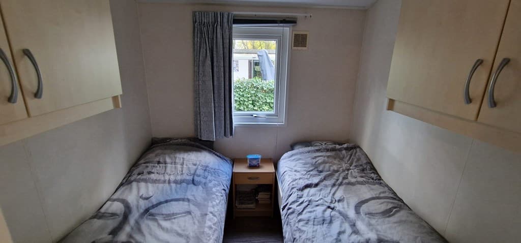 Slaapkamer met twee losse bedden, een klein nachtkastje en een raam met planten buiten.