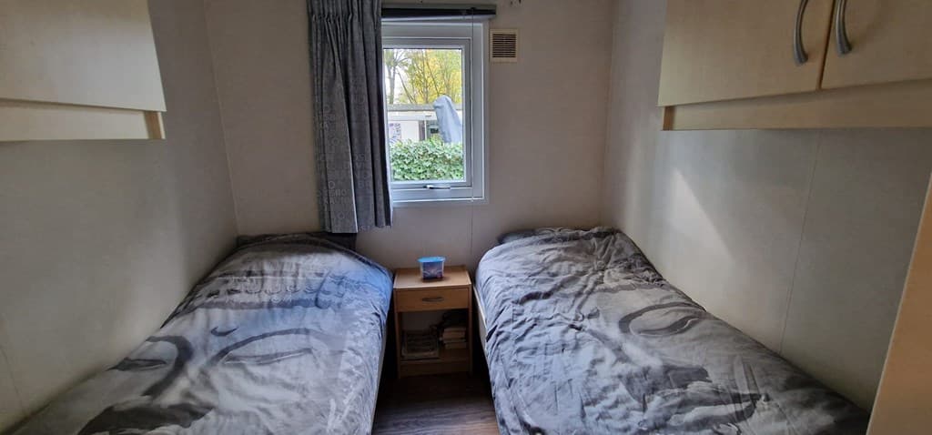 Slaapkamer met twee eenpersoonsbedden, een nachtkastje en een raam met uitzicht op buiten.