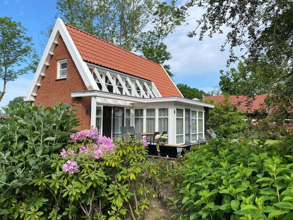 Vakantiehuis met rode dakpannen, een veranda en groene tuinplanten, gelegen in een rustige omgeving met bomen.