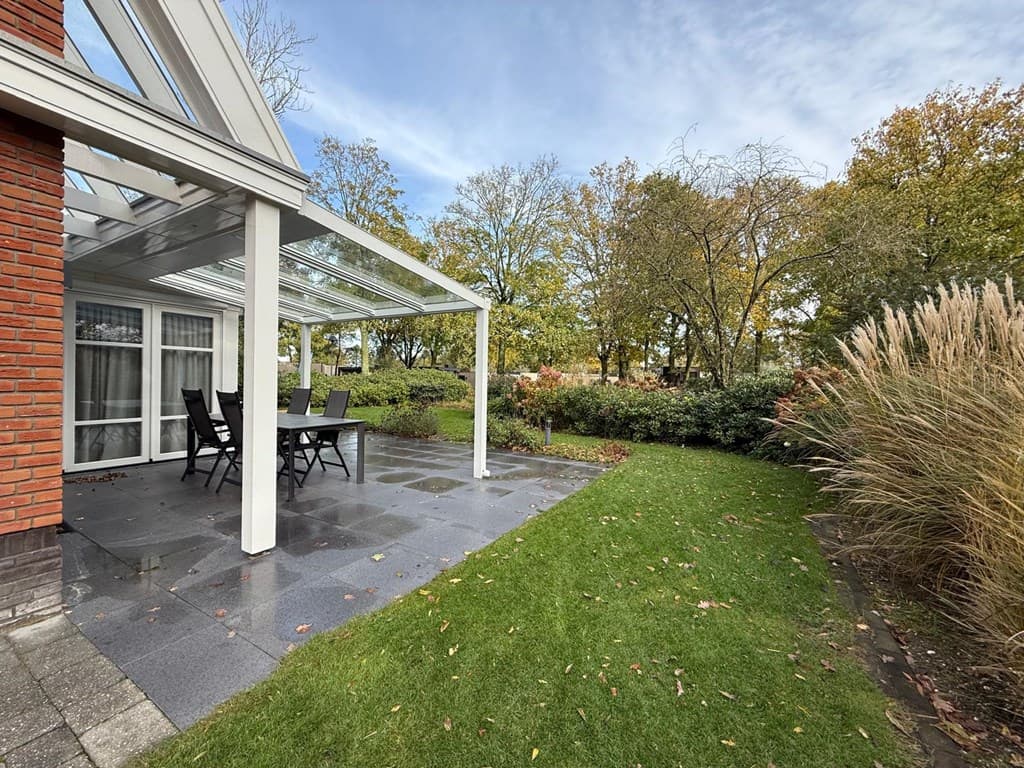 Buitenterras met tafel en stoelen, omringd door groen en bomen in EuroParcs Bad Hoophuizen.