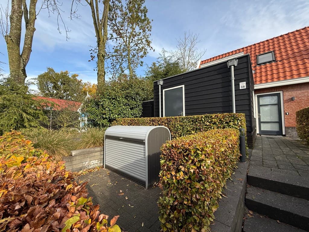 Buitenaanzicht van een woning met een zwart-witte gevel, een groene tuin en een kunststof berging bij de ingang.