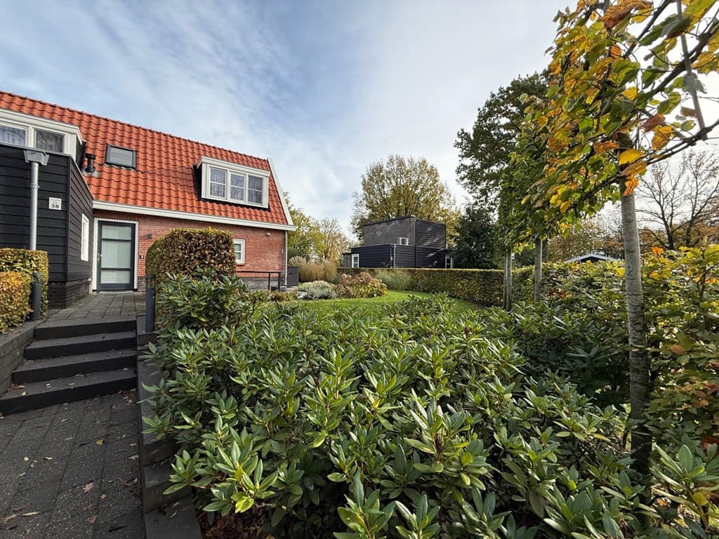 Tuin met groene begroeiing en stappen naar een woning met een rood pannendak en een moderne gevel