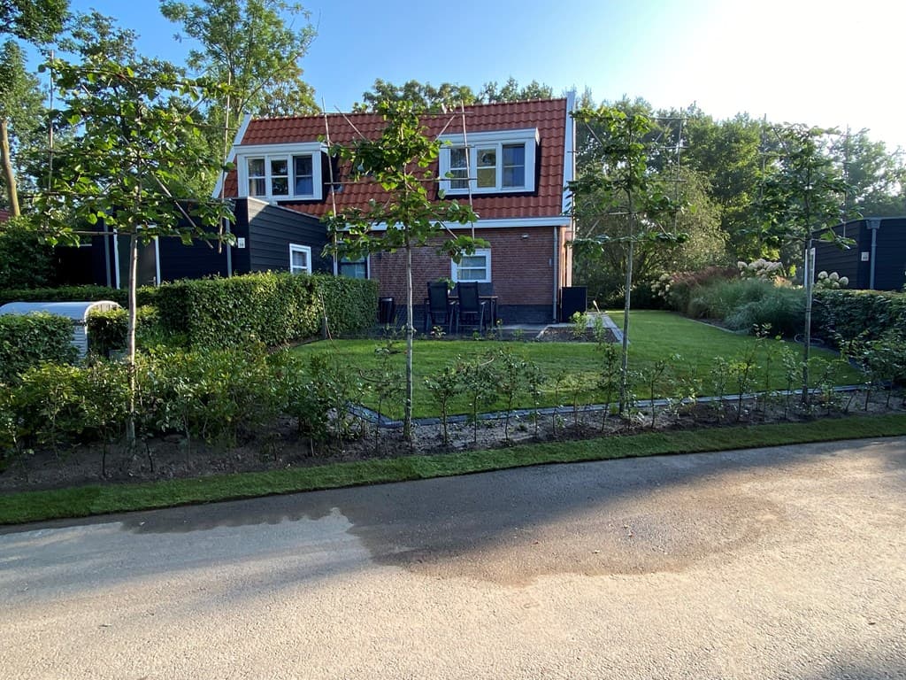 Zicht op een vakantiewoning met een tuin, grasveld en terras aan een rustige straat met groene begroeiing