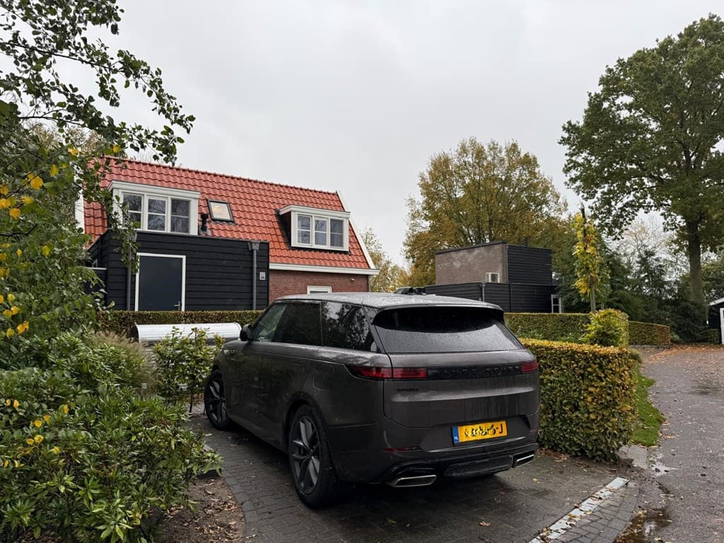 Zicht op een chalet met een rode dakpan, omliggende bomen en een grijze auto op een verhard pad