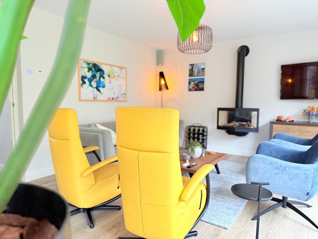 Zithoek met gele en blauwe stoelen, moderne haard, wanddecoratie en tv in een lichte woonkamer.